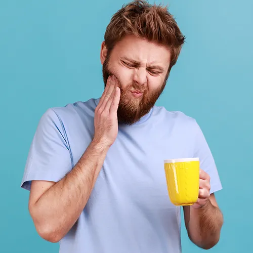 man holding a yellow mug in one hand and holding his cheek in pain in the other