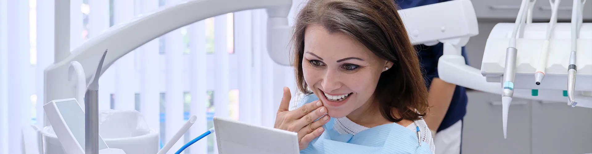 woman smiling into hand mirror while touching her chin 