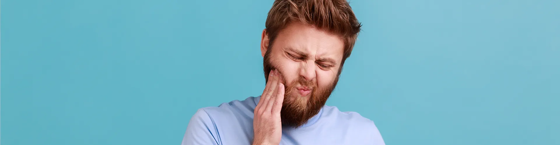 man holding a yellow mug in one hand and holding his cheek in pain in the other