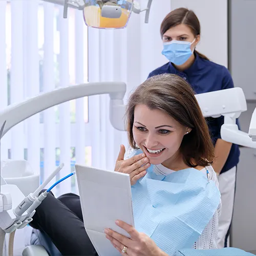 woman smiling into hand mirror while touching her chin 