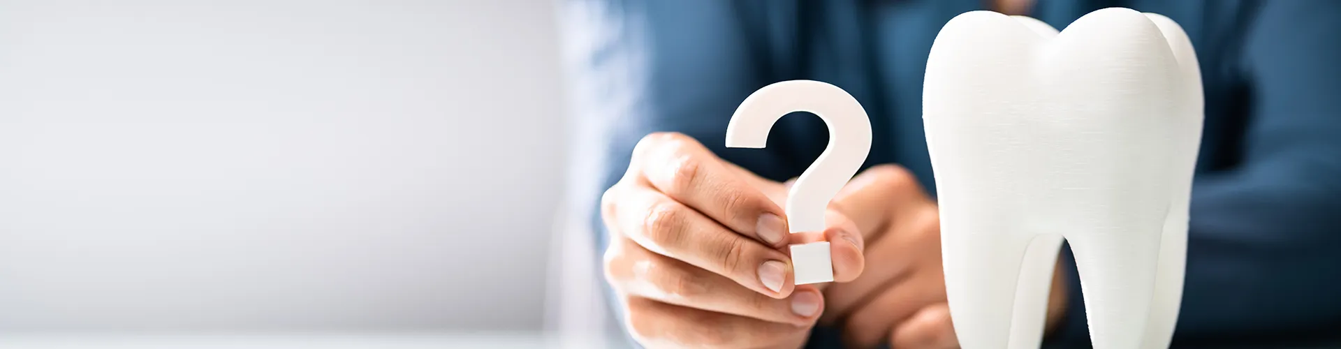 hand holding a white question mark beside a giant tooth model